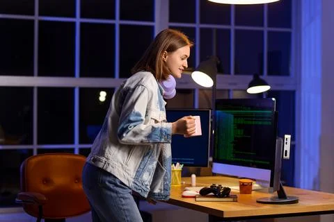 Happy female programmer with cup of coffee and computers working in office at Stock-Fotos