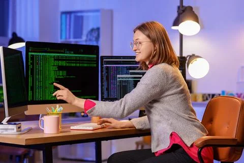 Happy female programmer with cup of coffee and computers working in office at Stock Photos