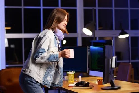 Happy female programmer with cup of coffee and computers working in office at Stock Photos
