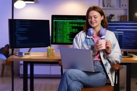 Happy female programmer with laptop, cup of coffee and computers working in o Stock-Fotos