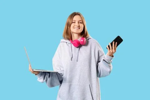 Happy female programmer with laptop, mobile phone and headphones on blue back Stock Photos