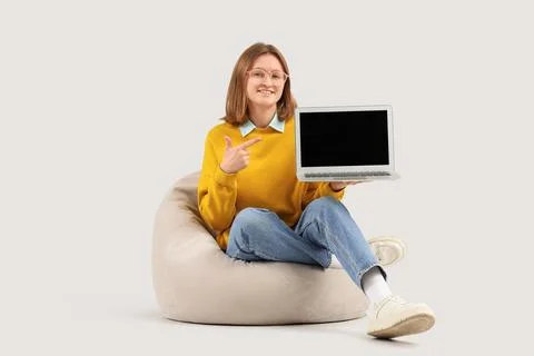 Happy female programmer pointing at laptop on beanbag chair against grey back Stock-Fotos