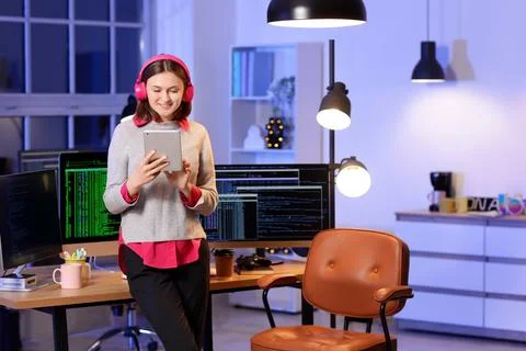 Happy female programmer with tablet and headphones working in office at night Stock-Fotos