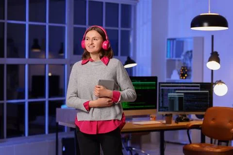 Happy female programmer with tablet and headphones working in office at night Stock-Fotos