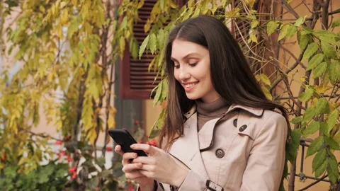 Happy female texting on cellphone while standing near the wall with plants. Stock-Footage 165207000