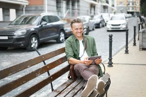 Happy freelancer man work using digital tablet sits on the bench outdoors in Stock-Fotos