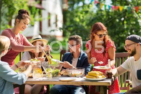 Happy friends having dinner at summer garden party Stock Photos