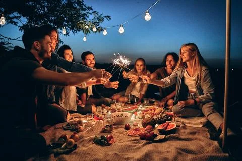Happy friends having fun with fire sparkles. Young people millennials camping Stock Photos