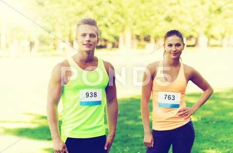 Happy friends or couple with racing badge numbers Stock Photos