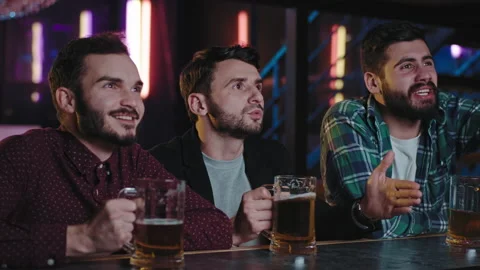 Happy friends in a pub while drinking some beer concentrated watching a football Stock Footage 135916041