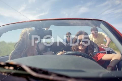 Happy friends pushing broken cabriolet car Stock Photos