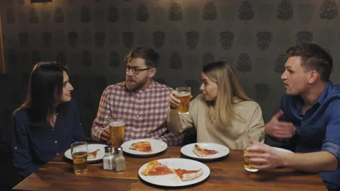Happy friends sit at the table in pub eat pizza watch tv and talk with each Video stock 151274941