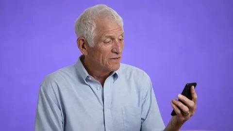 Happy fun elderly man 70s in blue shirt gets video call using mobile cell phone Stock Footage 213283622