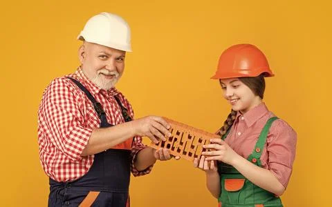 Happy girl and grandfather bricklayer in helmet on yellow background Stock Photos