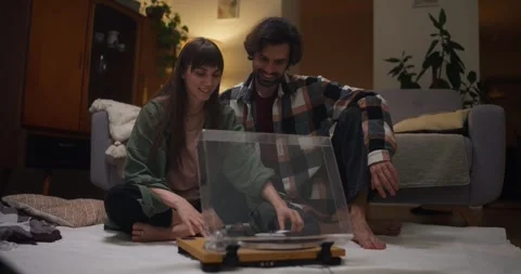 Happy girl and guy sitting near vinyl player and listening to music on record 動画素材 317628053