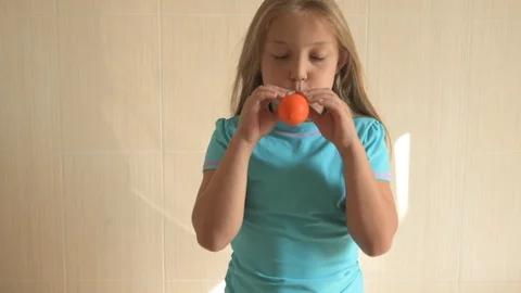 Happy girl in blue t-shirt inflates a bright orange ball in bathroom at home. Stock Footage