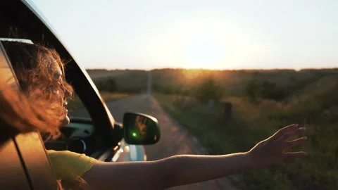 Happy girl in car window. Hair in wind. Girl travels by car. Hand in sun. Windy Stock Footage