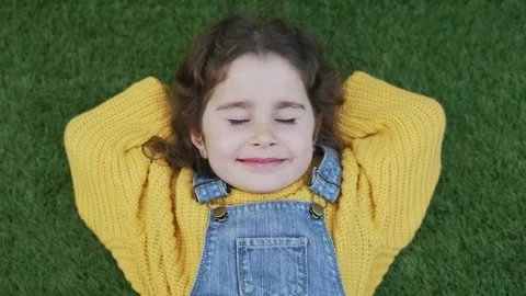 Happy girl with closed eyes stretched out on artificial turf enjoying good Stock Footage