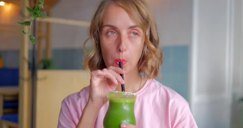Happy girl drinking green smoothie. Blond young woman holding detox drink Stock Footage