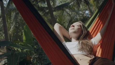 Happy girl enjoying sun rays lying in hammock on green tropical background Stock Footage 129213341