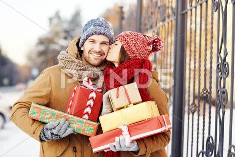 Happy girl with giftboxes kissing her boyfriend outdoors Stock Photos