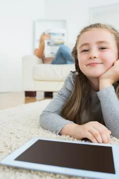 Happy girl with her tablet pc and her mother reading newspaper Stock Photos