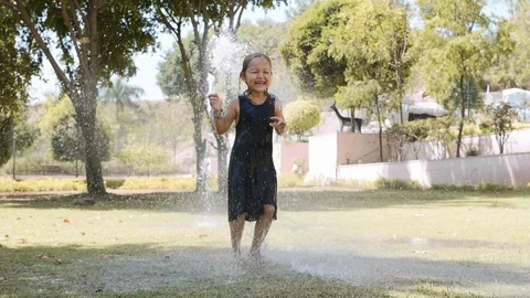 Happy girl is jumping in puddle under the water jet in park. Stock Footage
