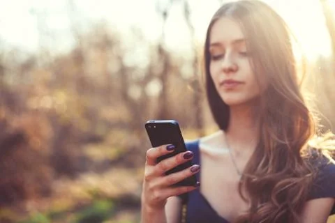 Happy girl reading message using her smart phone in the park. Focus on phone Stock Photos