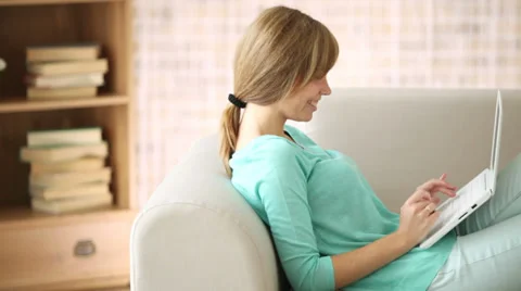 Happy girl relaxing on sofa using laptop holding credit card looking at camera Video stock 33851112