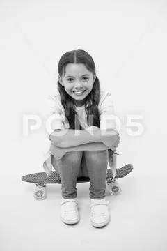 Happy girl sit on penny board on yellow background. Little child smile with long Stock Photos