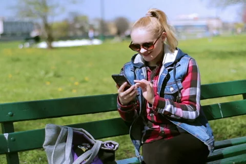 Happy girl sitting on the bench and using smartphone 動画素材 49869953