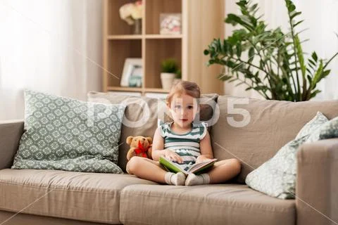 Happy girl sitting on sofa with book at home Stock-Fotos