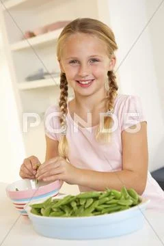 Happy girl splitting peas in kitchen Stock Photos