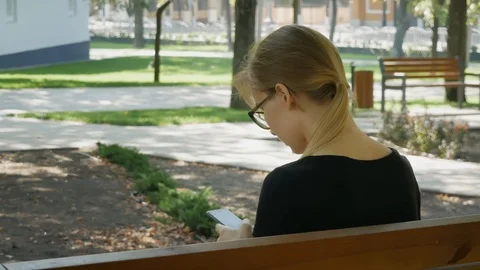 Happy girl student using a smart phone in a city park sitting on a bench, you Stock Footage 114178792
