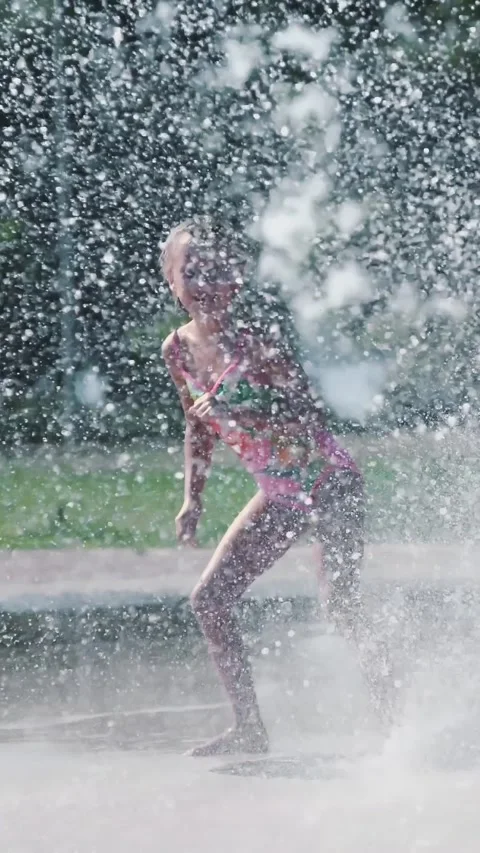 Happy girl in swimsuit, having fun between water splashes in fountain . Sunny Stock Footage 314886953