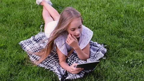 Happy girl using tablet pc lies on grass in the park Video stock 93307364