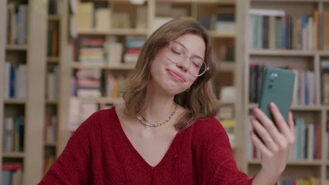 Happy girl waves while video chatting with phone at library, slomo Stock Footage 231457963