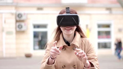 Happy girl wearing vr virtual reality headset glasses plays outside on street 動画素材 132676341