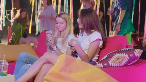 Happy girlfriends talking together with drinks on coach gossipping telling jokes Stock Footage 115355018