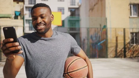 Happy good-looking African guy with basketball looking attentively at screen of Video stock 92055571