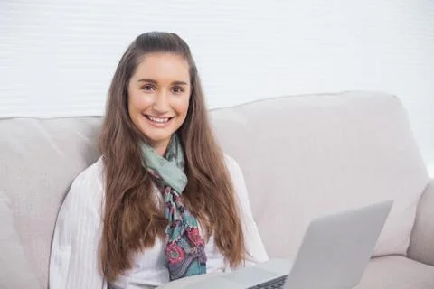 Happy gorgeous model using laptop sitting on sofa Foto stock