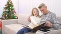 The happy grandfather and a girl watch an photo album near the christmas tree 4k or 4k+ Resolution