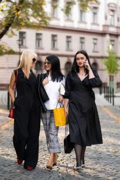 Happy group of three friends using a smart phone standing outdoors on the street Stock Photos