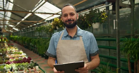 A happy guy with a beard in an apron holds a tablet in his hands and poses Stock Footage 280677158
