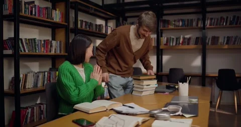 Happy guy brings a stack of books and sits near his female colleague while Stock Footage 313357117