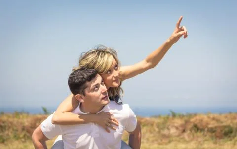 Happy guy carrying his girlfriend on back outdoors Stock Photos