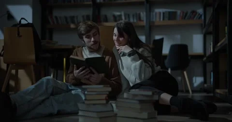 Happy guy chatting with his girlfriend and reading a book on the floor in a cozy Stock Footage 313357381