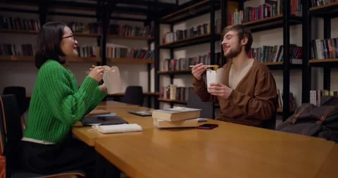 Happy guy in glasses communicates with his Asian female colleague during lunch Stock Footage 313356654