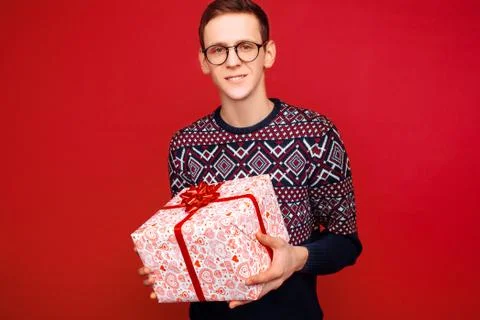 Happy guy in glasses with a gift box in hands on red background Stock Photos