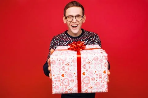 Happy guy in glasses with a gift box in hands on red background Stock Photos
